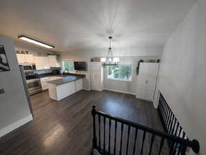 Kitchen with a chandelier, appliances with stainless steel finishes, a peninsula, new Dekton dark countertops, and dark wood-style flooring