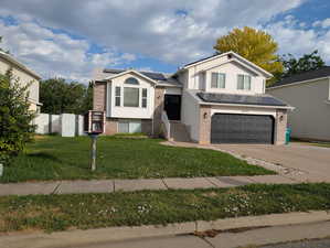 View of front of house featuring brick siding, concrete driveway, an attached garage, and paid off solar panels