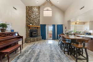 Dining space with a wood stove, high vaulted ceiling, ceiling fan, and light wood-style flooring