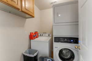 Washroom featuring cabinet space and stacked washing machine and dryer