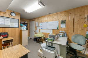 Office area featuring carpet, wood walls, and a textured ceiling
