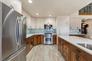 Kitchen featuring stainless steel appliances, light countertops, light wood-type flooring, tasteful backsplash, and brown cabinets