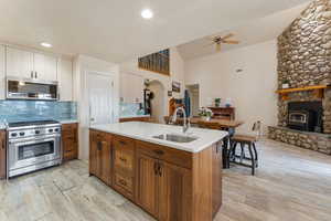 Kitchen with stainless steel appliances, a ceiling fan, a wood stove, a kitchen island with sink, and backsplash