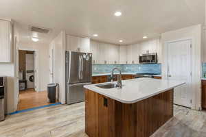Kitchen with stacked washer / dryer, appliances with stainless steel finishes, light countertops, light wood-type flooring, and recessed lighting