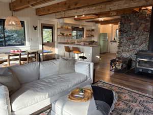 Open floor plan with wood burning stove, decorative stone wall, exposed wood beams on ceiling