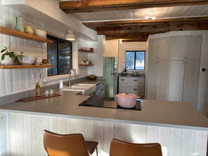 Remodeled kitchen with open shelves, refrigerator, a breakfast bar, a wood ceiling with exposed beams, and a breakfast bar area
