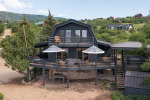 Rear view of house featuring a gambrel roof, log veneer siding, a deck with mountain view, stairs, and a metal roof