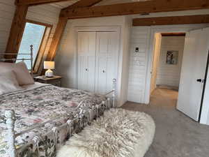 Carpeted bedroom featuring wooden walls, a closet, and beamed ceiling