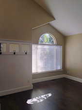 Spare room featuring dark wood-type flooring and vaulted ceiling