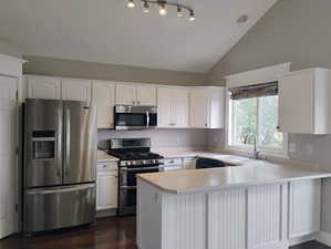 Kitchen featuring appliances with stainless steel finishes, light countertops, white cabinetry, a peninsula, and lofted ceiling