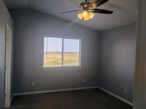 Spare room featuring vaulted ceiling, ceiling fan, and dark colored carpet
