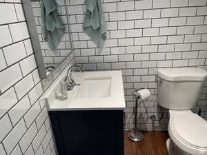 Bathroom featuring tile walls, vanity, wood finished floors, and tasteful backsplash