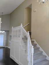 Stairs with a chandelier, a towering ceiling, and wood finished floors