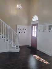 Foyer entrance featuring dark wood-style floors, a chandelier, stairs, and a high ceiling