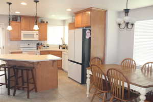 Kitchen featuring white appliances, light countertops, a kitchen island, a kitchen bar, and light tile patterned floors