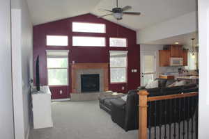 Living room with ceiling fan, carpet, lofted ceiling, plenty of natural light, and a fireplace
