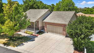 View of front of house with roof with shingles, a garage, brick siding, and driveway