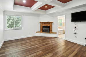 Unfurnished living room featuring coffered ceiling, hardwood / wood-style flooring, ornamental molding, beam ceiling, and a glass covered fireplace