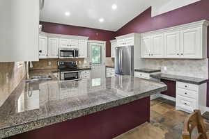 Kitchen with tile counters, vaulted ceiling, appliances with stainless steel finishes, a peninsula, and backsplash