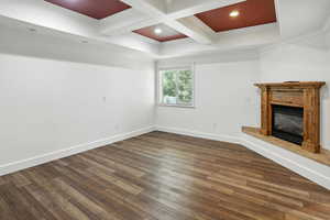 Unfurnished living room with coffered ceiling, crown molding, beam ceiling, dark wood-style flooring, and a glass covered fireplace