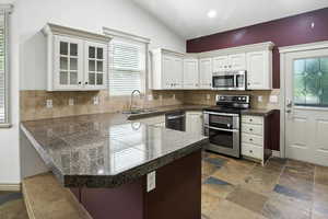 Kitchen with tile counters, stainless steel appliances, vaulted ceiling, backsplash, and a peninsula