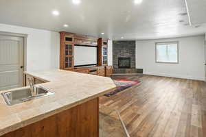 Kitchen with tile counters, a stone fireplace, brown cabinets, hardwood / wood-style flooring, and recessed lighting