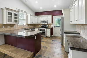 Kitchen featuring a peninsula, appliances with stainless steel finishes, backsplash, stone tile floors, and tile countertops