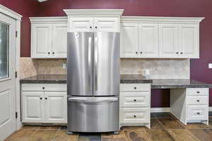 Kitchen featuring freestanding refrigerator, tile counters, backsplash, and white cabinetry