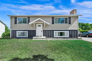 Raised ranch with board and batten siding, a front yard, and a chimney