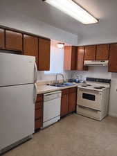 Kitchen with white appliances, light countertops, brown cabinets, and under cabinet range hood