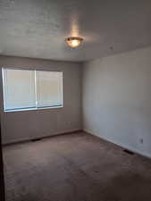 Carpeted spare room with a textured ceiling and baseboards