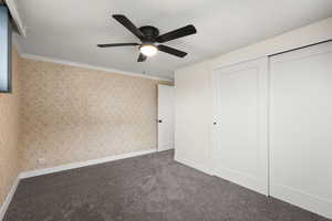 Unfurnished bedroom with a textured ceiling, dark colored carpet, wallpapered walls, ornamental molding, and ceiling fan