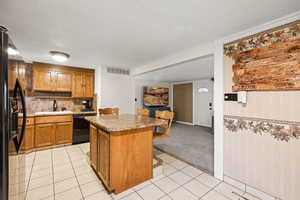 Kitchen with brown cabinets, light tile patterned floors, a textured ceiling, a center island, and stainless steel refrigerator with ice dispenser