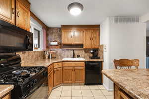 Kitchen featuring black appliances, brown cabinets, backsplash, light tile patterned floors, and a textured ceiling