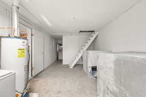 Finished below grade area featuring gas water heater, light colored carpet, washer / dryer, stairway, and a textured ceiling
