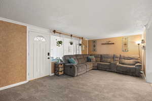 Carpeted living room with ornamental molding, a textured ceiling, and wallpapered walls
