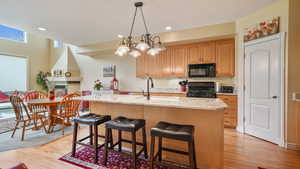 Kitchen with black appliances, light wood-style flooring, a kitchen island with sink, light granite counters, and recessed lighting