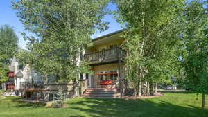 Rear view of property with a balcony, a lawn, stairway, and a wooden deck