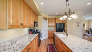 Kitchen with black appliances, light wood-type flooring, light granite countertops, a chandelier, and recessed lighting
