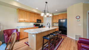 Kitchen featuring black appliances, a kitchen breakfast bar, light stone countertops, light wood-style flooring, and recessed lighting