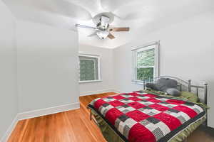 Main level Unit A primary Bedroom with wood finished floors, multiple windows, a ceiling fan, and a textured ceiling