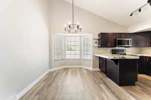 Kitchen with light wood finished floors, stainless steel microwave, open shelves, a chandelier, and pendant lighting