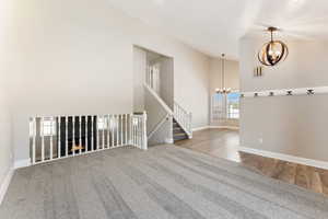 Carpeted empty room with a chandelier, wood finished floors, and a high ceiling