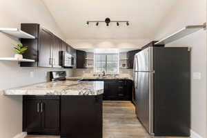 Kitchen with open shelves, stainless steel appliances, vaulted ceiling, a peninsula, and light wood-type flooring