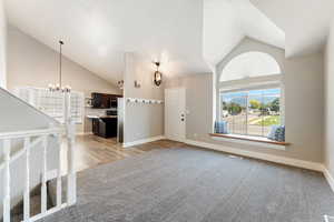 Empty room with a chandelier, high vaulted ceiling, light carpet, and light wood-type flooring