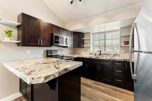 Kitchen with open shelves, appliances with stainless steel finishes, lofted ceiling, light wood finished floors, and dark brown cabinetry