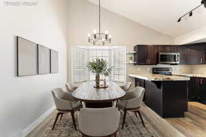 Dining room featuring a chandelier, light wood-style floors, high vaulted ceiling, and rail lighting