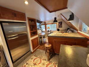 Kitchen with stainless steel refrigerator, brown cabinets, light tile patterned floors, vaulted ceiling, and recessed lighting