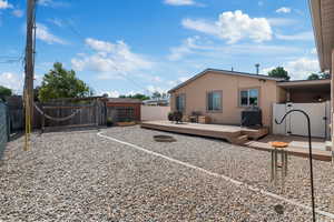 Back of house featuring a wooden deck, fire pit, rock garden and a raised garden beds