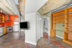 Kitchen with open shelves, finished concrete flooring, stainless steel appliances, track lighting, and wall chimney range hood